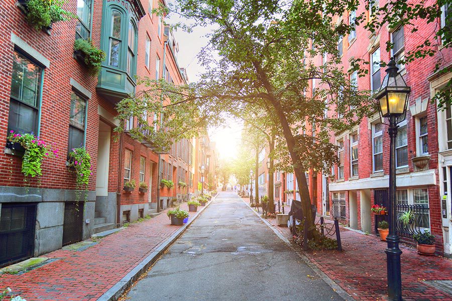 About Our Agency - View Looking Down a Row of Brick Homes in Boston, Massachusetts, the Sun Beaming Down the Center of the Street, Brick Walkways and Street Lamps Lining the Street