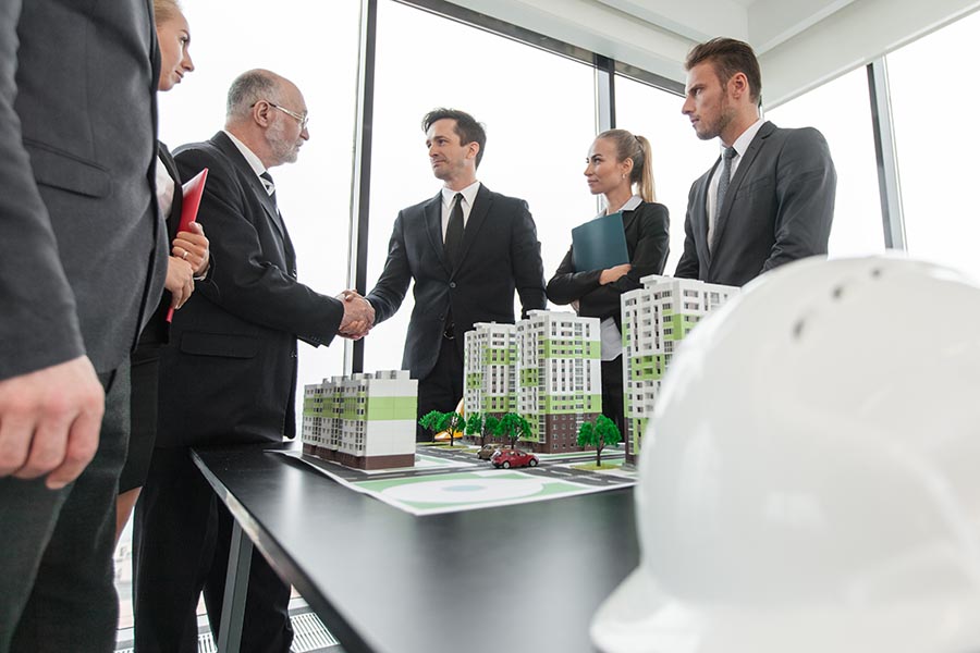 Specialized Business Insurance - Business Associates Shake Hands Over Scale Model of a Planned Condominium Community, a White Hardhat in the Foreground